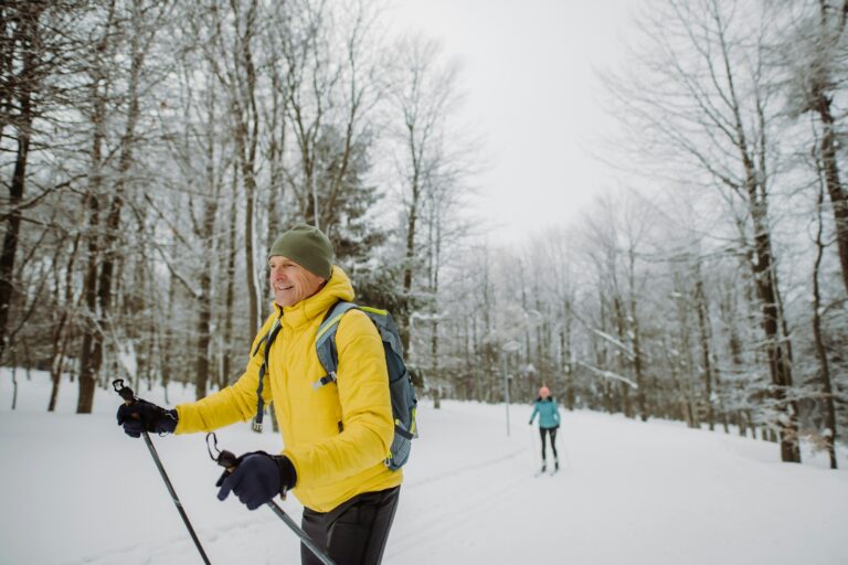 Senior man doing cross country skiing in front of snowy forest.