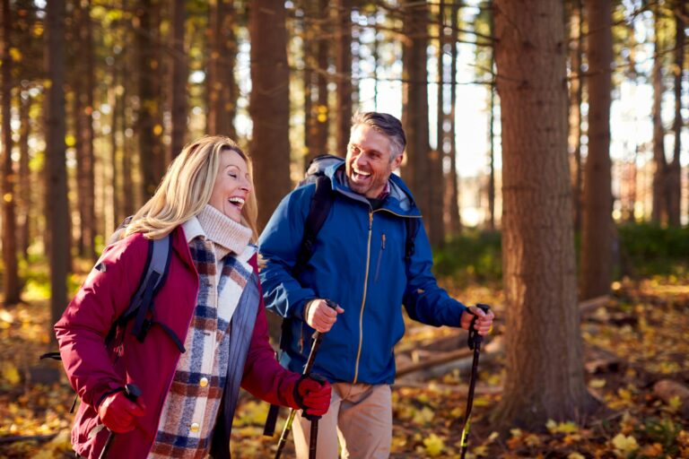 Side View Of Mature Retired Couple Walking Through Fall Or Winter Countryside Using Hiking Poles